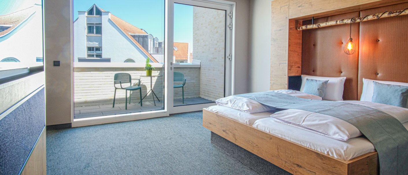 Modernes Hotelzimmer mit Doppelbett, stilvoller Beleuchtung und Zugang zu einer Terrasse mit zwei St&uuml;hlen und Tisch., &copy; 13 6 Design GmbH (Judenhof 10, 89073 Ulm)