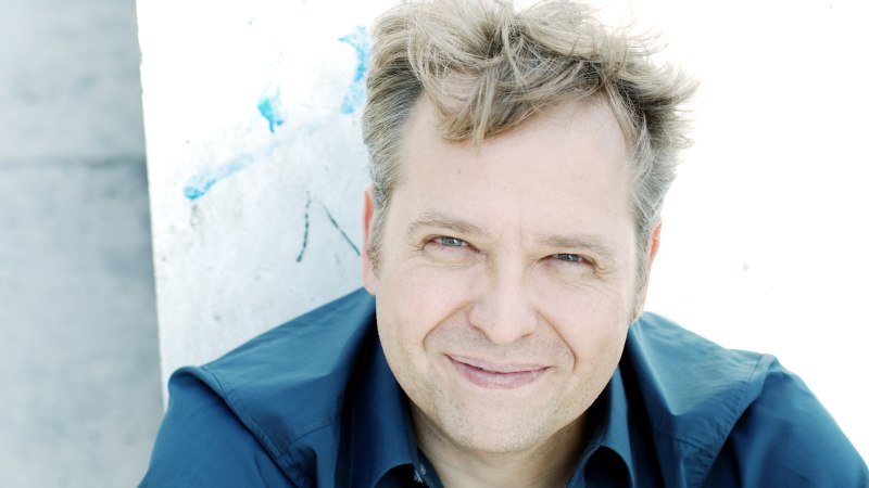 Ein Mann mit blonden Haaren und blauem Hemd l&auml;chelt in die Kamera. Der Hintergrund ist hell und leicht strukturiert., &copy; Soany Guigand