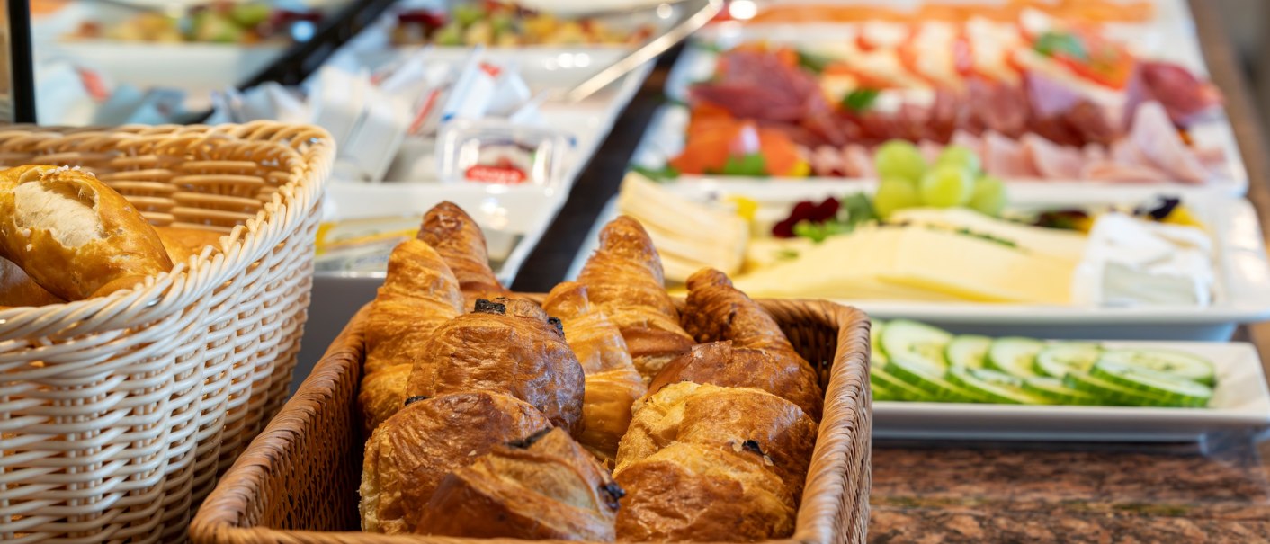 A breakfast buffet with croissants, bread rolls and various cold cuts on plates., © PLAZA INN Rieker Stuttgart Hauptbahnhof