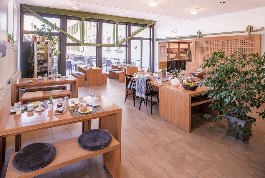 Bright breakfast room with wooden tables, plants and large windows. Cozy atmosphere with laid tables and cushions., &copy; ECOINN Hotel am Campus