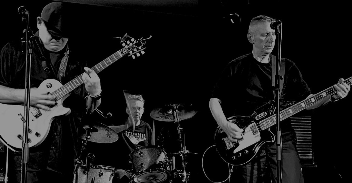 Eine Band spielt auf der B&uuml;hne. Zwei Gitarristen und ein Schlagzeuger sind in Aktion. Das Bild ist in Schwarz-Wei&szlig; gehalten., &copy; Herz Rhythmus Maschine