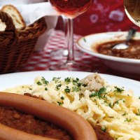 A plate of lentils, spaetzle and sausages on a red and white checkered tablecloth. A basket of bread and a glass of wine in the background., &copy; Stuttgart-Marketing GmbH