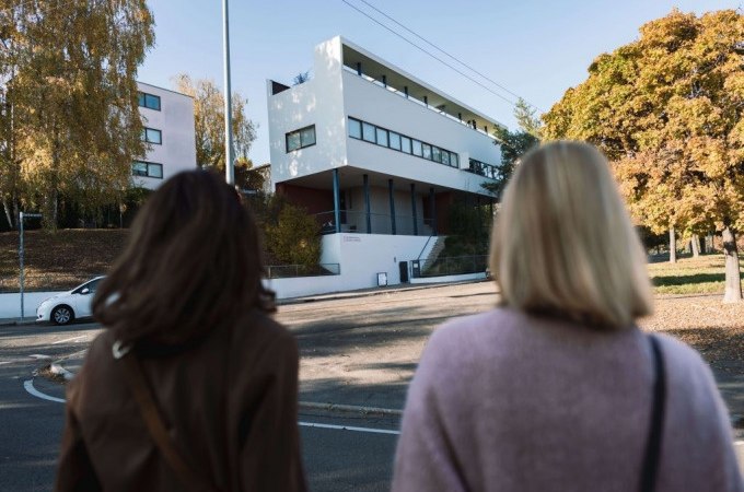 Zwei Personen stehen vor einem modernen Gebäude in der Weissenhofsiedlung, umgeben von herbstlichen Bäumen., © Stuttgart-Marketing GmbH, Ingolf Pompe Zwei Personen stehen vor einem modernen Gebäude in der Weissenhofsiedlung, umgeben von herbstlichen Bäumen., © Stuttgart-Marketing GmbH, Ingolf Pompe