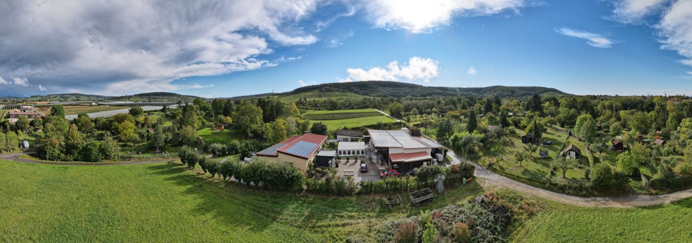Luftaufnahme des Weinguts Ei&szlig;ele mit Geb&auml;uden, Feldern und B&auml;umen. Im Hintergrund H&uuml;gel und blauer Himmel mit Wolken., &copy; Weingut Ei&szlig;ele