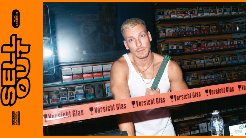 Ein Mann in einem Tanktop steht hinter einer Theke mit Zigarettenpackungen. Ein Band mit der Aufschrift 'Vorsicht Glas' ist im Vordergrund., &copy; links im Bild