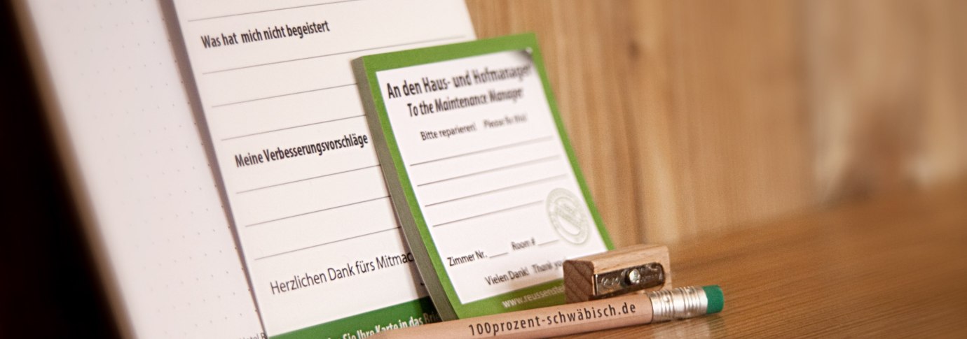 Ein Bleistift mit der Aufschrift "100prozent-schw&auml;bisch.de", ein Anspitzer und Formulare f&uuml;r Meinungen und Reparaturanfragen auf einem Holztisch., &copy; TOMAS