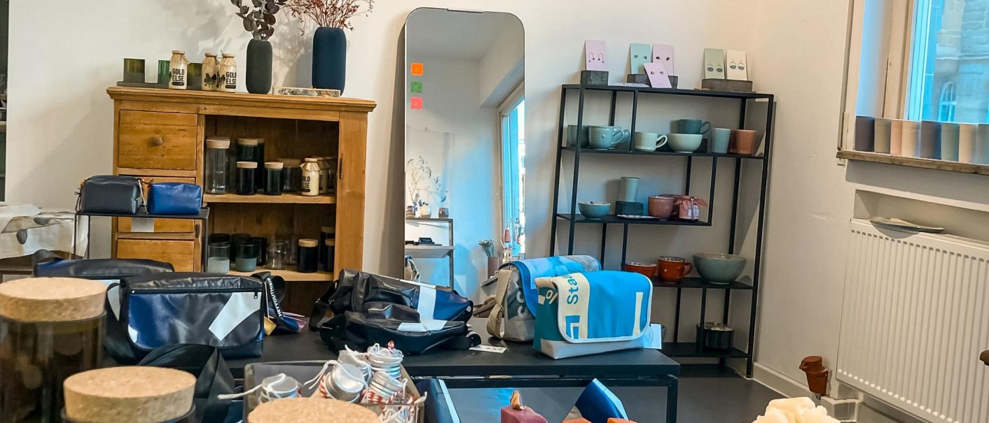 Ein Raum mit Holzschrank, Spiegel, Regalen mit Keramik und Taschen. Fenster mit blauem Licht. Dekorative Elemente auf dem Schrank., © Südstatt, Stuttgart Ein Raum mit Holzschrank, Spiegel, Regalen mit Keramik und Taschen. Fenster mit blauem Licht. Dekorative Elemente auf dem Schrank., © Südstatt, Stuttgart