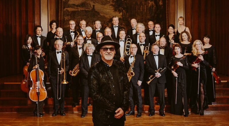 Die SWR Big Band und Paul Carrack posieren in eleganter Kleidung mit Instrumenten in einem stilvollen Raum., © C² CONCERTS GmbH Die SWR Big Band und Paul Carrack posieren in eleganter Kleidung mit Instrumenten in einem stilvollen Raum., © C² CONCERTS GmbH
