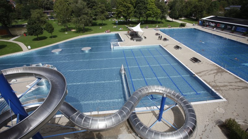 Freibad Rosental mit gro&szlig;er Wasserrutsche, mehreren Schwimmbecken und umliegenden Gr&uuml;nfl&auml;chen. Menschen entspannen auf der Wiese., &copy; Stuttgarter B&auml;der