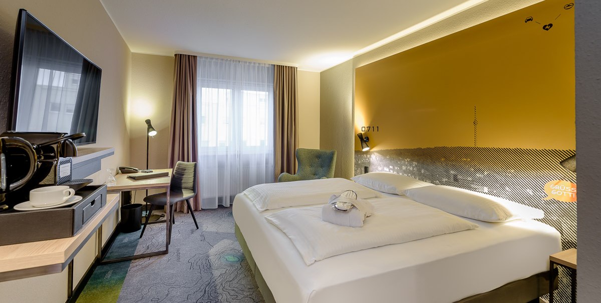 Modernes Hotelzimmer mit Doppelbett, Schreibtisch, Fernseher und Kaffeemaschine. Helle Farben und stilvolle Dekoration schaffen eine einladende Atmosphäre., © TOMAS