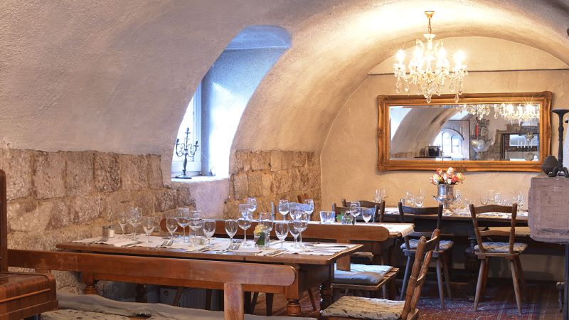 Cozy dining room with covered wooden tables, chandelier, mirror and rustic stone walls. Elegant atmosphere with candles and flowers., &copy; FreCla Gastronomiebetriebe GmbH
