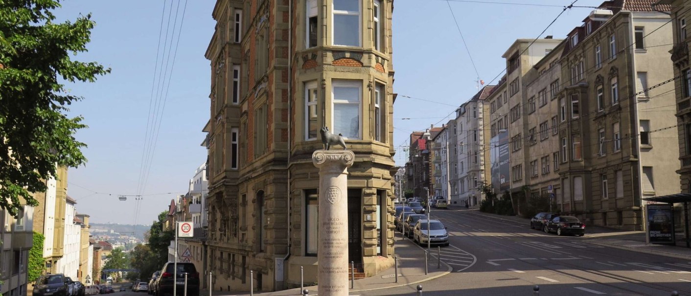 Das Loriot-Denkmal am Eugensplatz in Stuttgart zeigt eine Säule mit einer Skulptur darauf. Im Hintergrund sind historische Gebäude und eine Straße zu sehen., © Stuttgart-Marketing GmbH Das Loriot-Denkmal am Eugensplatz in Stuttgart zeigt eine Säule mit einer Skulptur darauf. Im Hintergrund sind historische Gebäude und eine Straße zu sehen., © Stuttgart-Marketing GmbH
