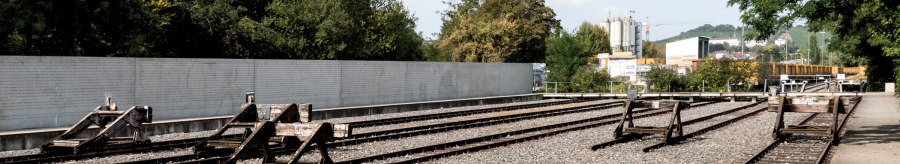 Gedenkst&auml;tte mit stillgelegten Bahngleisen, umgeben von B&auml;umen und einer Mauer. Ein ruhiger Ort des Erinnerns., &copy; Foto-Kunst Andreas Keller
