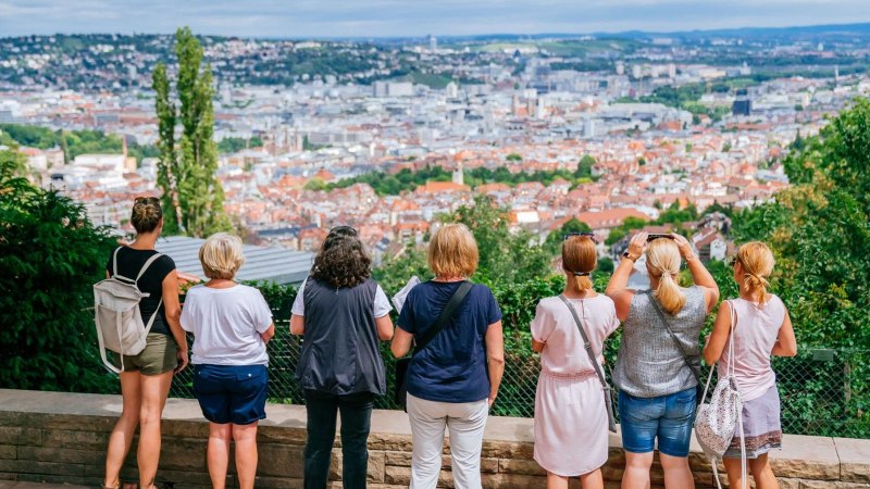 Eine Gruppe von Menschen steht auf einer Plattform und blickt auf eine Stadtlandschaft mit roten Dächern und grünen Hügeln im Hintergrund., © Thomas Niedermüller