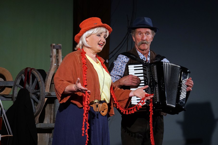 Eine Frau mit rotem Hut singt, während ein Mann neben ihr Akkordeon spielt. Im Hintergrund sind Wagenräder zu sehen., © Katja Ritter Eine Frau mit rotem Hut singt, während ein Mann neben ihr Akkordeon spielt. Im Hintergrund sind Wagenräder zu sehen., © Katja Ritter