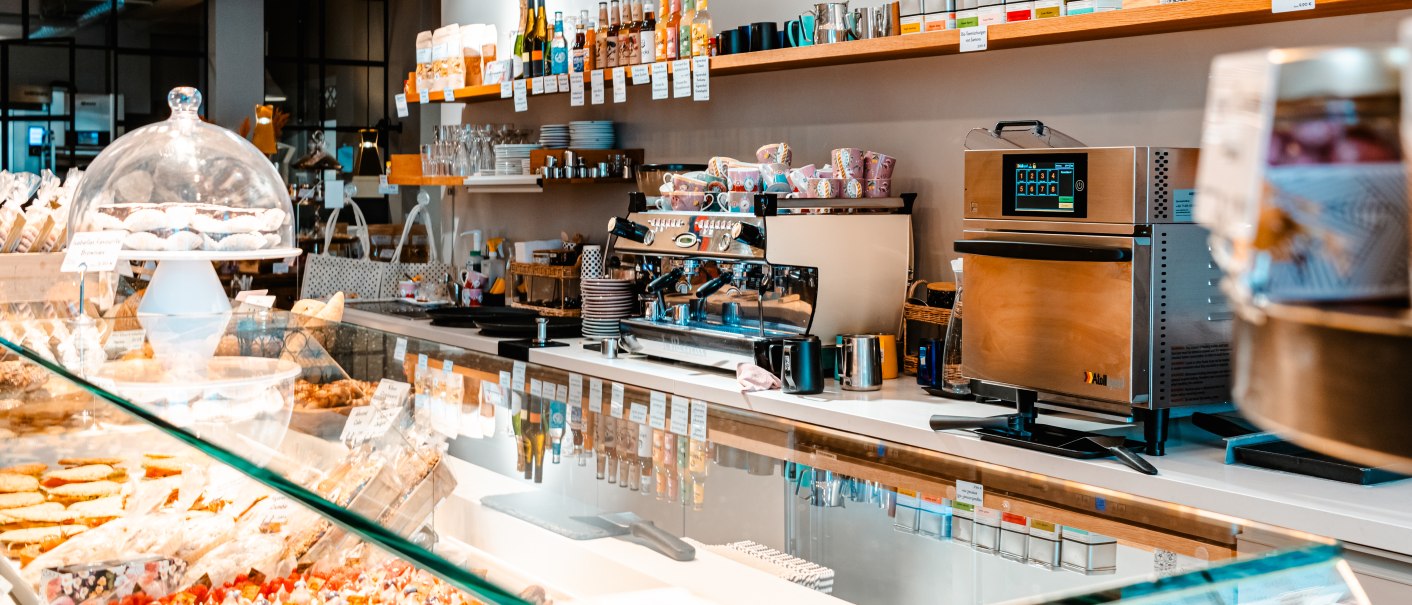 Eine moderne Bäckerei mit glutenfreien Produkten, Kaffeemaschine und Regalen voller Backwaren. An der Wand steht "Glutenfreie Patisserie seit 2014"., © SMG_Sarah Schmid