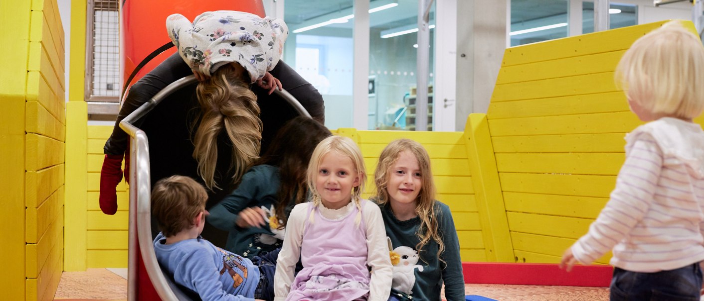 Kinder spielen auf einer Rutsche in einem Indoor-Spielplatz. Die Umgebung ist bunt mit gelben W&auml;nden und Spielger&auml;ten., &copy; Julia Ochs