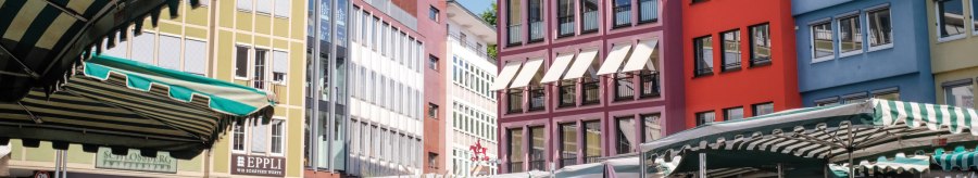Bunte Geb&auml;ude und Marktst&auml;nde auf einem Marktplatz, mit einem Kirchturm im Hintergrund unter blauem Himmel., &copy; SMG, trickytine