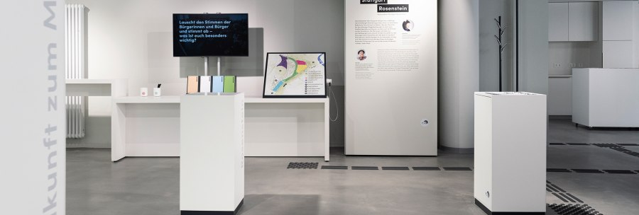 Moderne Ausstellung mit weißen Podesten, Infotafeln und einem Bildschirm. Thema: Stimmen zu Stuttgart Rosenstein. Minimalistisches Design., © Stadt Stuttgart / Dominique Brewing