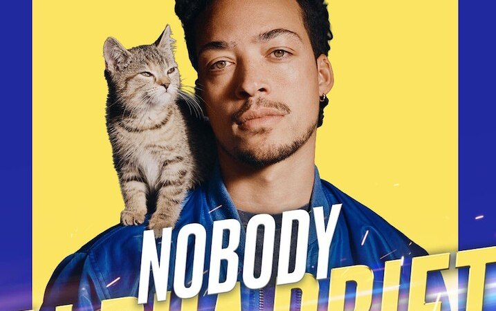 Ein Mann mit einer Katze auf der Schulter vor einem gelben Hintergrund. Der Text 'Aurel Mertz Nobody Alpha Drift' ist prominent platziert., &copy; Theaterhaus Stuttgart e.V.