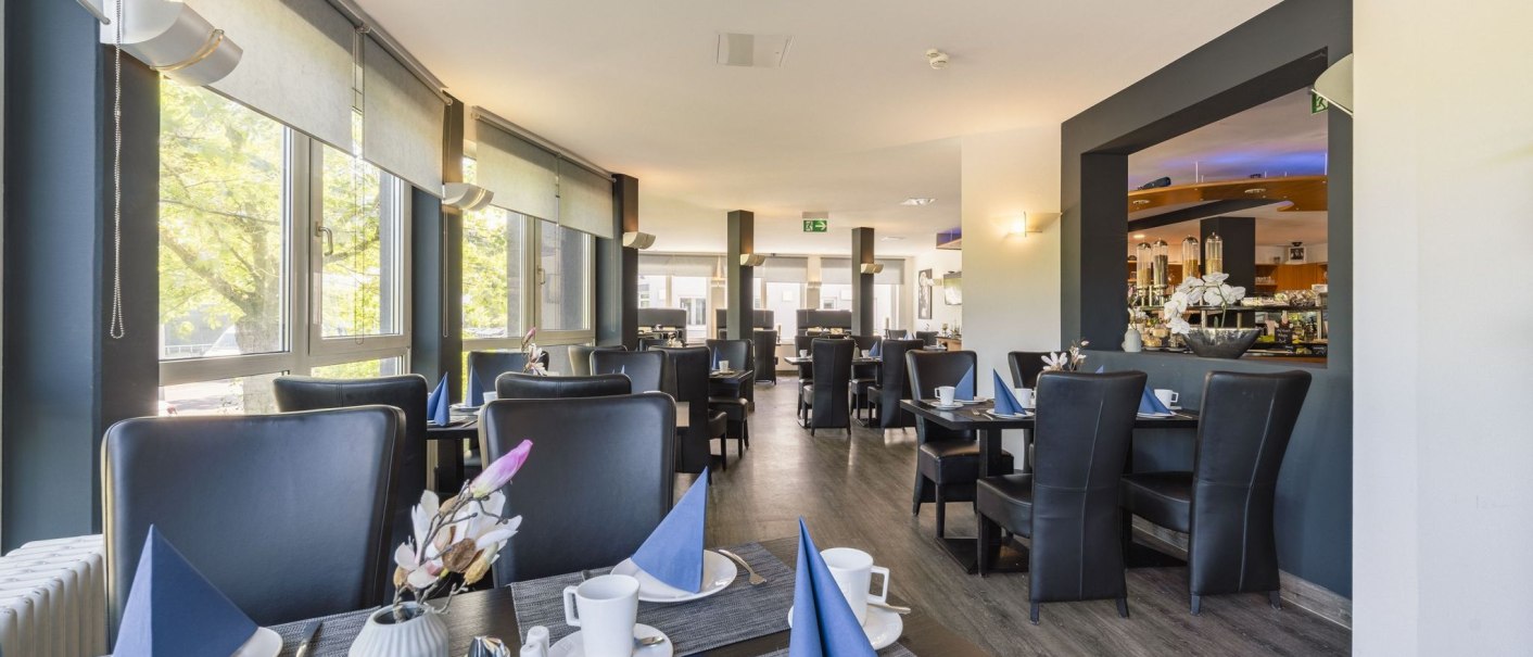 Modern breakfast area with laid tables, blue napkins and large windows that let in plenty of light., &copy; Plaza INN Stuttgart-Filderstadt