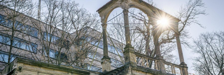 The ruins of the Neues Lusthaus with stone arches, surrounded by bare trees. Rays of sunlight break through the branches. A modern building in the background., &copy; Stuttgart-Marketing GmbH, Sarah Schmid