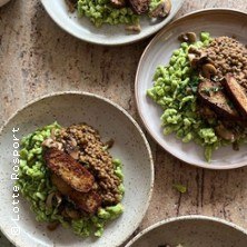 Mehrere Teller mit veganen Gerichten, darunter Linsen, gebratener Tofu und gr&uuml;ne Beilagen, auf einem Holztisch arrangiert., &copy; links im Bild