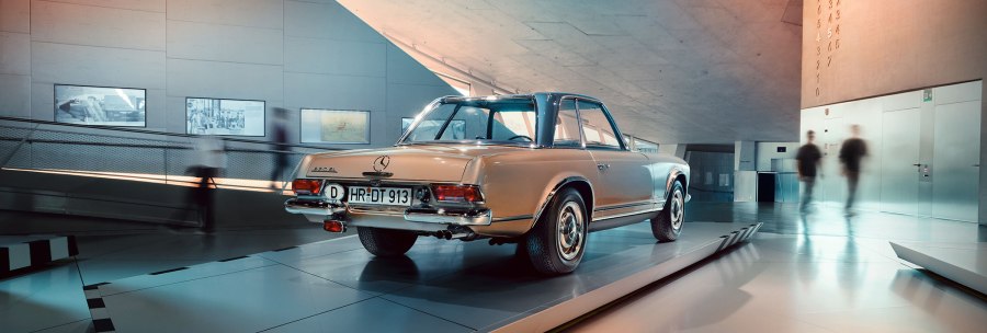 Ein Mercedes-Benz 280 SL steht im modernen Museum ausgestellt. Menschen gehen im Hintergrund vorbei. Die Architektur ist futuristisch., © Mercedes-Benz Heritage GmbH Ein Mercedes-Benz 280 SL steht im modernen Museum ausgestellt. Menschen gehen im Hintergrund vorbei. Die Architektur ist futuristisch., © Mercedes-Benz Heritage GmbH