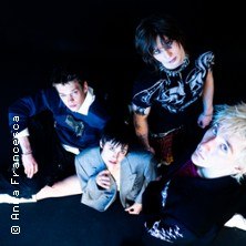 Four people in stylish clothes pose in a dark room and look into the camera. The scene looks dynamic and modern., &copy; see on the left