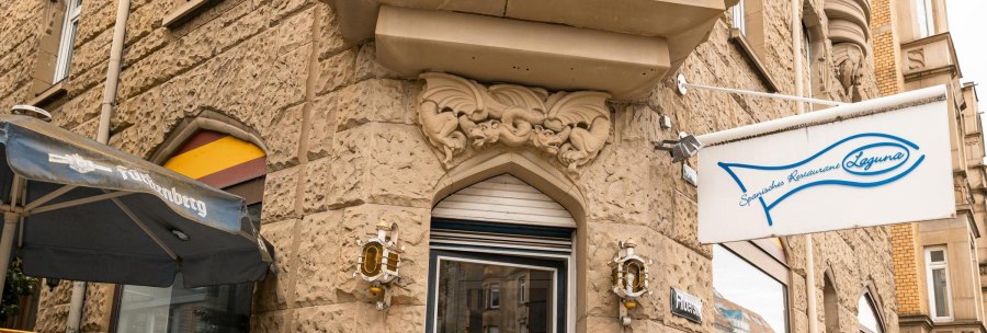 Eingang eines spanischen Restaurants namens Laguna mit Fisch-Logo. Sandsteinfassade mit dekorativen Elementen und einem Sonnenschirm., &copy; SMG, Sarah Schmid