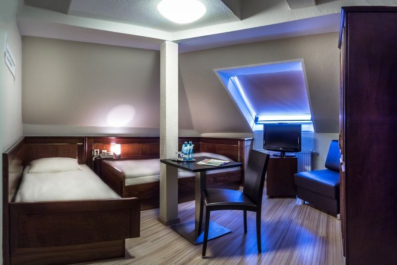 Twin room with two single beds, table, chair and TV under a sloping roof. Modern furnishings with wooden furniture and skylight., &copy; TOMAS