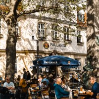 Menschen sitzen im Außenbereich eines Paulaner-Restaurants. Ein großer Baum spendet Schatten, und ein Brunnen ist im Vordergrund zu sehen., © SMG Stuttgart Marketing GmbH - Sarah Schmid Menschen sitzen im Außenbereich eines Paulaner-Restaurants. Ein großer Baum spendet Schatten, und ein Brunnen ist im Vordergrund zu sehen., © SMG Stuttgart Marketing GmbH - Sarah Schmid