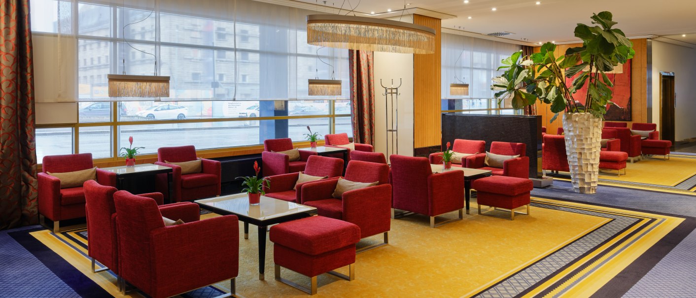 Elegant lobby bar with red armchairs, yellow carpet and large plants. Large windows let in plenty of light., © Steigenberger Graf Zeppelin