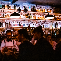 Eine stimmungsvolle Bar mit beleuchteten Flaschenregalen. Menschen unterhalten sich, während ein Barkeeper Getränke zubereitet., © Stuttgart-Marketing GmbH, Sarah Schmid Eine stimmungsvolle Bar mit beleuchteten Flaschenregalen. Menschen unterhalten sich, während ein Barkeeper Getränke zubereitet., © Stuttgart-Marketing GmbH, Sarah Schmid