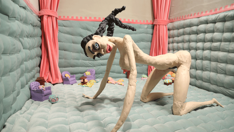 A kneeling sculpture in a pastel-colored room with pink curtains and small furniture., © VG Bild-Kunst, Bonn 2024, Courtesy the artist and  Lisson Gallery A kneeling sculpture in a pastel-colored room with pink curtains and small furniture., © VG Bild-Kunst, Bonn 2024, Courtesy the artist and  Lisson Gallery