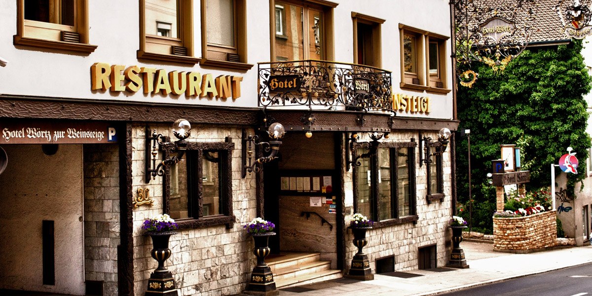 The entrance to the Hotel Zur Weinsteige, featuring decorative elements, large windows, and restaurant signage. Flowers adorn the entrance area., &copy; Hotel Zur Weinsteige