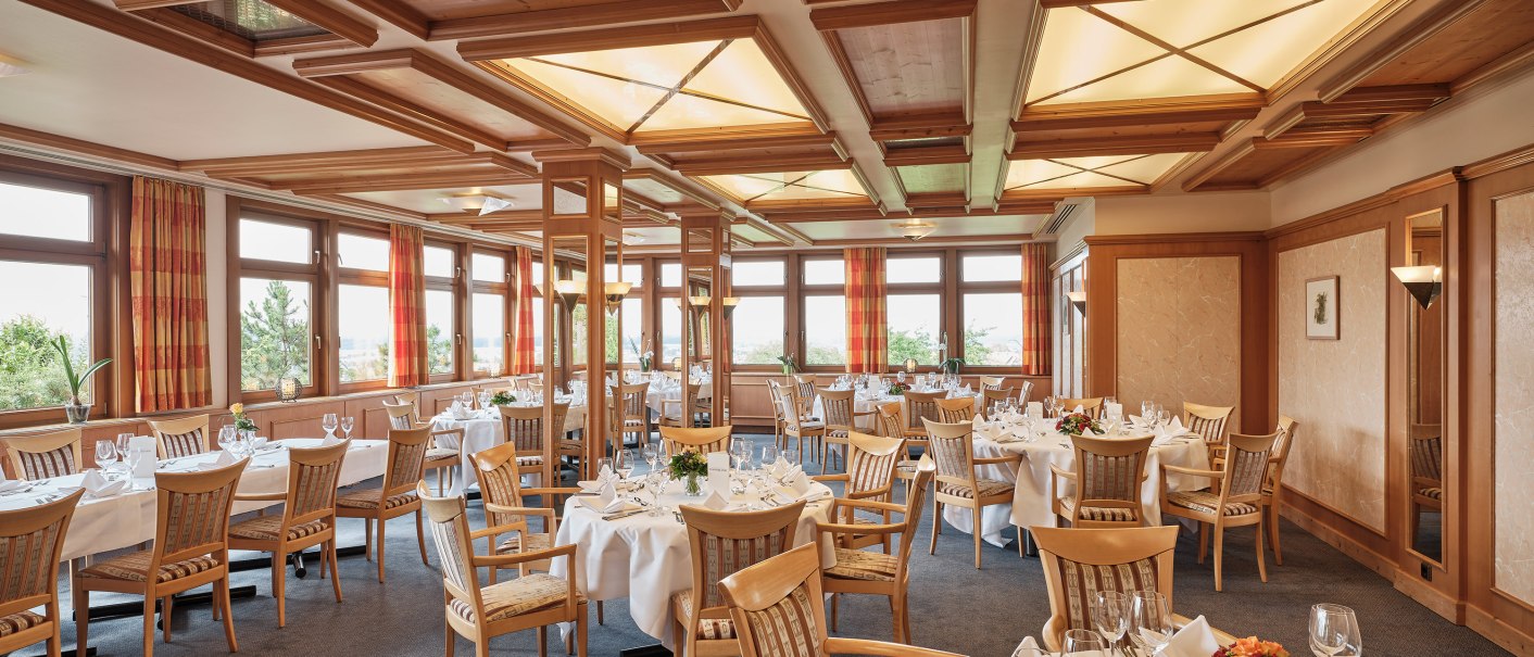 Eleganter Speisesaal mit Holzelementen, gedeckten Tischen und großen Fenstern. Die Decke ist mit Holzpaneelen verziert., © Badhotel Restaurant Stauferland