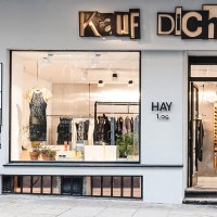 Schaufenster eines Modegeschäfts namens 'Kauf Dich Glücklich' mit Kleidung und Pflanzen dekoriert., © Kauf Dich Glücklich GmbH Schaufenster eines Modegeschäfts namens 'Kauf Dich Glücklich' mit Kleidung und Pflanzen dekoriert., © Kauf Dich Glücklich GmbH