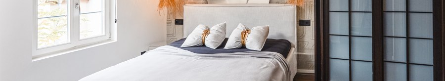 Modernes Hotelzimmer mit gro&szlig;em Bett, Wandbild einer Frau, zwei H&auml;ngelampen und Holzfu&szlig;boden., &copy; Zauberlehrling