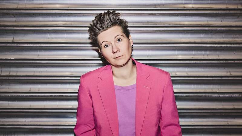 Eine Person mit kurzem Haar tr&auml;gt einen pinken Blazer und ein lila Shirt. Sie steht vor einer metallischen Wand und schaut direkt in die Kamera., &copy; Rosenau Kultur e.V.