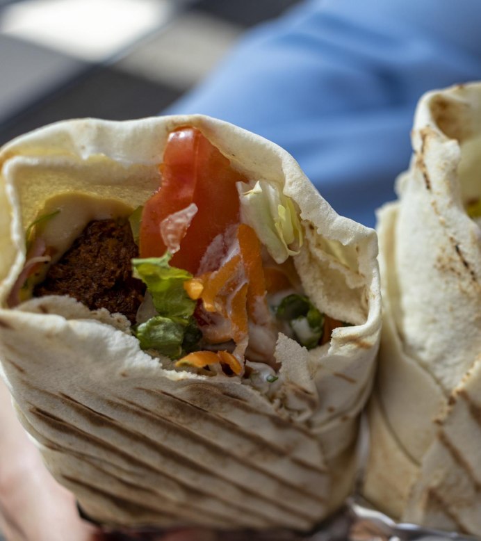 Two freshly grilled wraps filled with falafel, salad, tomatoes, and yoghurt sauce, held in hand. The crispy flatbreads have distinct grill marks. In the blurred background, the blue sleeves of the person holding them are visible., © Stuttgart-Marketing GmbH, Sarah Schmid