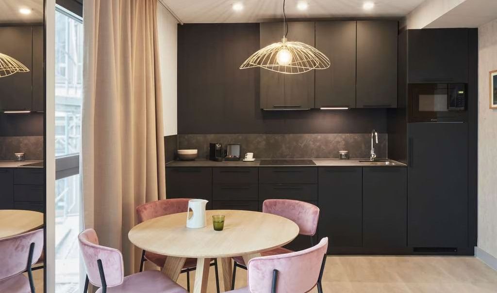 Modern kitchen with black fitted kitchen, round wooden table and pink chairs. Large windows and stylish lighting., © Adagio Modern kitchen with black fitted kitchen, round wooden table and pink chairs. Large windows and stylish lighting., © Adagio