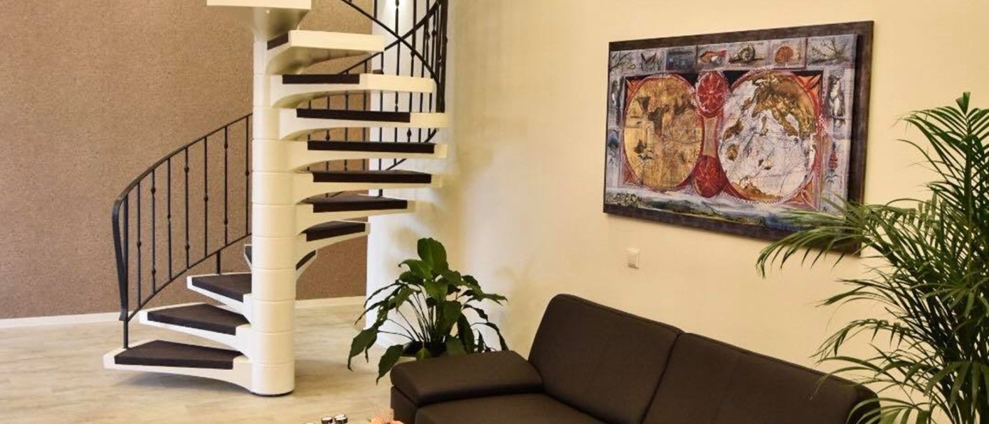 Modern lobby with spiral staircase, black sofa, coffee table and plants. A painting hangs on the wall and a chandelier hangs from the ceiling., © TOMAS Modern lobby with spiral staircase, black sofa, coffee table and plants. A painting hangs on the wall and a chandelier hangs from the ceiling., © TOMAS