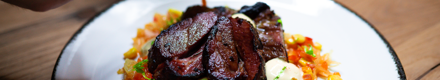 An artfully arranged dish with meat, vegetables and sauce on a white plate. One hand holds a spoon over the plate., &copy; Cara Schmid