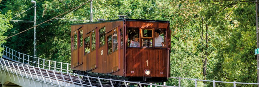 Eine historische Standseilbahn mit Holzverkleidung fährt eine geneigte Strecke entlang, umgeben von dichtem Grün., © TMBW, Gregor Lengler