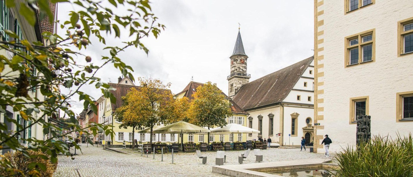 Göppingen's downtown area, featuring historic buildings, a church tower, and a square with trees and places to sit. An autumnal atmosphere., © SMG Stuttgart Marketing GmbH - Sarah Schmid Göppingen's downtown area, featuring historic buildings, a church tower, and a square with trees and places to sit. An autumnal atmosphere., © SMG Stuttgart Marketing GmbH - Sarah Schmid