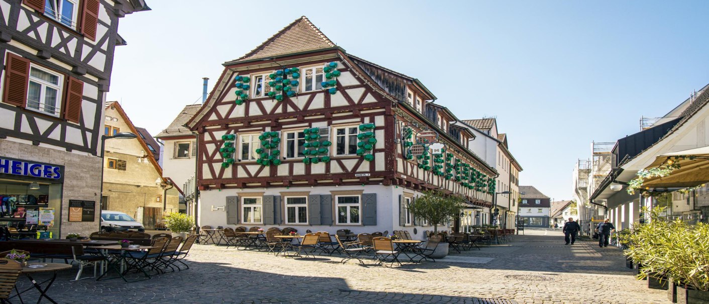 Half-timbered house in Kirchheim unter Teck with blue shutters and street café. Cobblestones and clear skies in the background., © SMG Stuttgart Marketing GmbH - Sarah Schmid