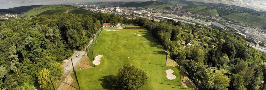 Luftaufnahme eines Golfplatzes in Stuttgart, umgeben von Bäumen und Hügeln, mit der Stadt im Hintergrund unter einem bewölkten Himmel., © GolfKultur Stuttgart