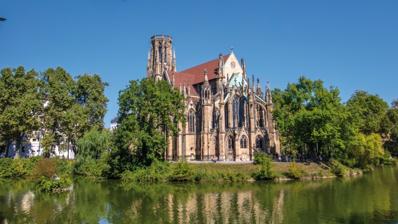 Die Johanneskirche am Feuersee in Stuttgart, umgeben von B&auml;umen und reflektiert im Wasser, bei klarem, sonnigem Wetter., &copy; SMG Achim Mende