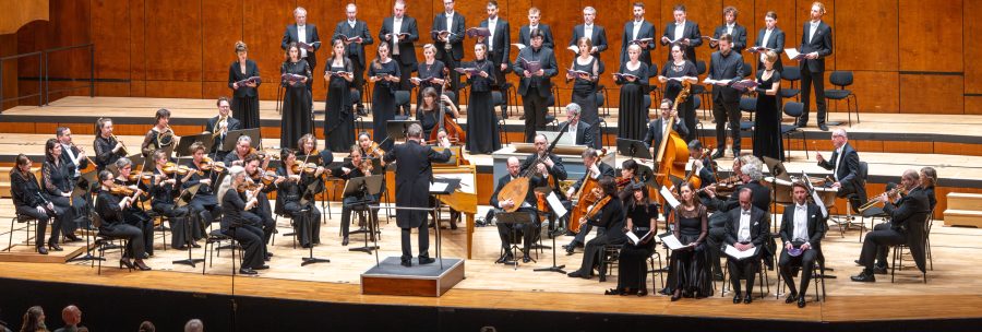 Ein Orchester und Chor in formeller Kleidung f&uuml;hren auf einer B&uuml;hne ein klassisches Konzert auf. Der Dirigent steht vor dem Orchester., &copy; Holger Schneider